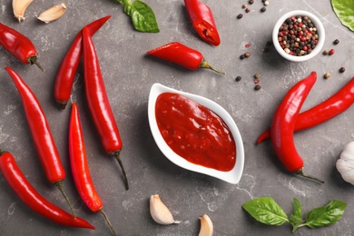 Flat lay composition with gravy boat of hot chili sauce and different spices on gray background