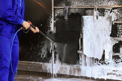Worker cleaning auto mats with high pressure water jet at car wash, closeup