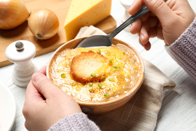 Woman eating tasty homemade french onion soup at white wooden table, closeup