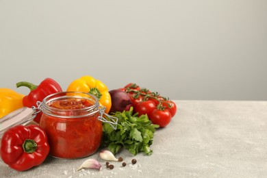 Photo of Glass jar of delicious canned lecho and fresh ingredients on light grey table. Space for text
