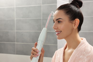 Photo of Woman using high frequency darsonval device in bathroom, space for text