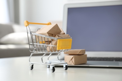 Internet shopping. Laptop and small cart with boxes on table indoors