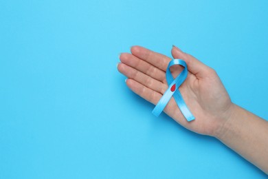 Woman holding light blue ribbon with paper blood drop on color background, top view and space for text. Diabetes awareness