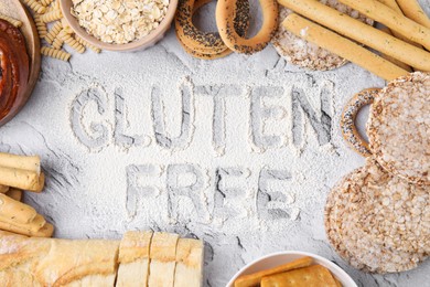 Different products and phrase Gluten free written with flour on light grey table, flat lay