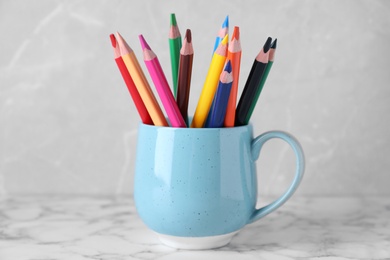 Colorful pencils in cup on white marble table against grey background