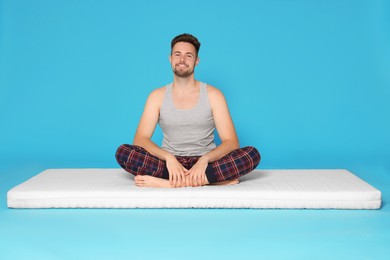 Smiling man sitting on soft mattress against light blue background