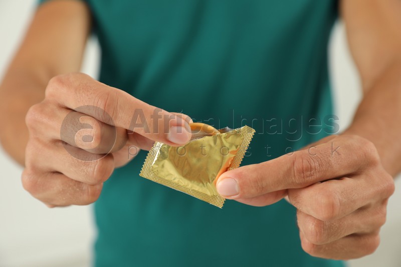 Young man holding condom on light background, closeup. Safe sex concept