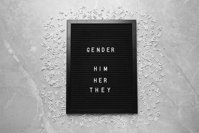 Black board with words Gender, Him, Her, They and letters on grey marble table, flat lay