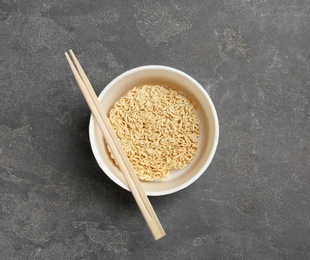 Photo of Cup of instant noodles with chopsticks on grey background, top view