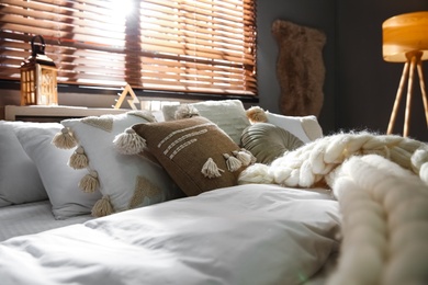 Photo of Bed with cozy knitted blanket and cushions near window in room. Interior design