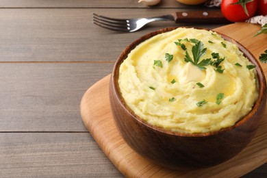 Photo of Bowl of freshly cooked mashed potatoes with parsley served on wooden table, closeup. Space for text