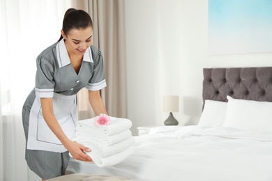 Chambermaid putting fresh towels on bed in hotel room. Space for text