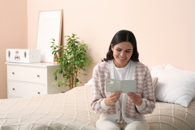 Photo of Young woman with greeting card on bed in room, space for text