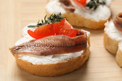 Photo of Delicious sandwiches with cream cheese, anchovy and tomatoes on wooden board, closeup