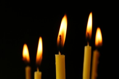 Photo of Burning church candles on black background, closeup