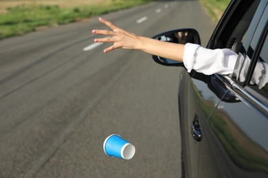 Driver throwing away paper cup from car window. Garbage on road