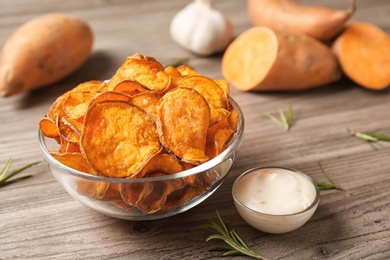 Delicious sweet potato chips in bowl, rosemary and sauce on table