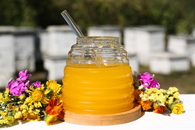 Delicious fresh honey and beautiful flowers on white wooden table in apiary