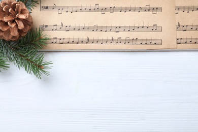 Christmas music sheets and fir tree branch and space for text on white wooden background, top view