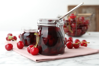 Jars of pickled cherries and fresh fruits on white marble table