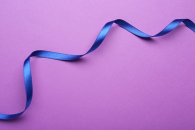 Beautiful blue ribbon on purple background, top view. Space for text