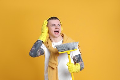 Handsome young man with floor brush singing on orange background