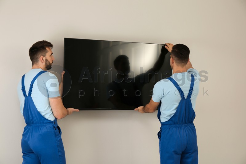 Professional technicians installing modern flat screen TV on wall indoors