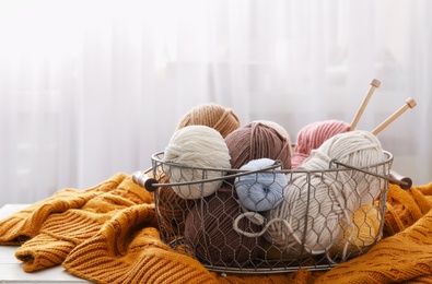 Soft woolen yarns with knitting needles and sweater on table indoors, space for text