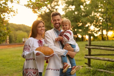 Photo of Happy cute family in embroidered Ukrainian shirts with korovai bread on sunny day