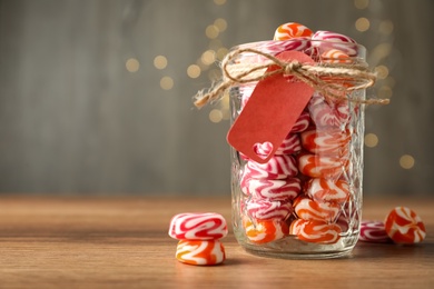 Color hard candies in glass jar on wooden table. Space for text