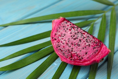 Delicious cut red pitahaya fruit and palm leaf on light blue wooden table, closeup