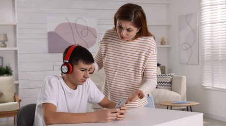 Mother scolding her son while he listening music in headphones at home. Teenager problems