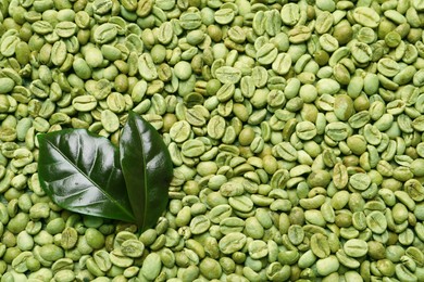 Many green coffee beans and leaves as background, top view