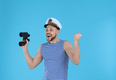 Happy sailor with binoculars on light blue background
