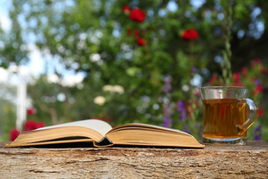 Open book with glass cup of tea on wooden table in garden