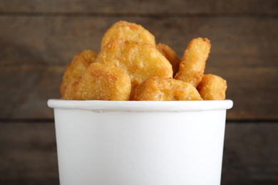 Photo of Bucket with tasty chicken nuggets on wooden background, closeup
