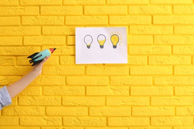 Woman holding toy rocket near yellow brick wall with lamps drawing, closeup. Startup concept