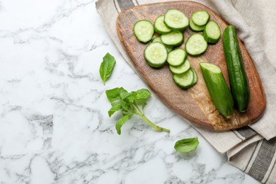 Fresh ripe cucumbers and basil on white marble table, flat lay. Space for text
