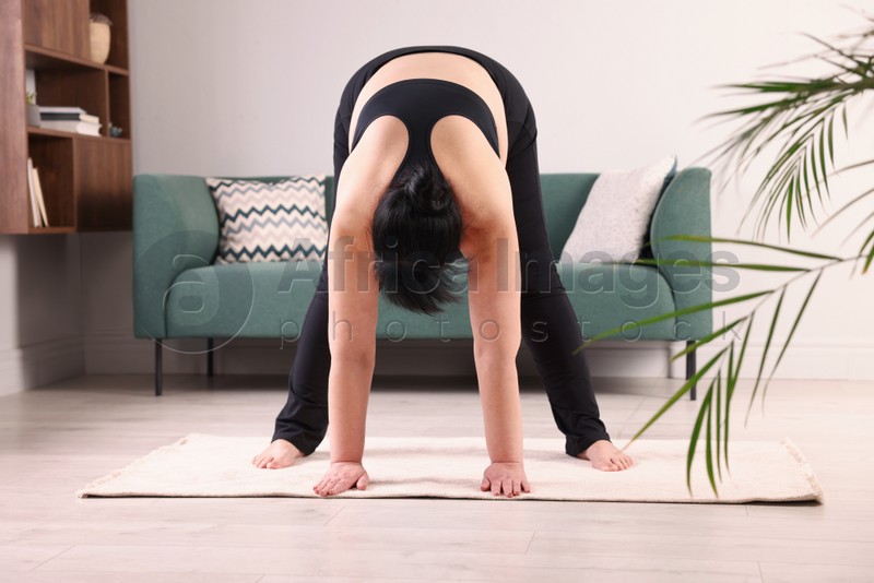 Photo of Overweight mature woman stretching on rug at home