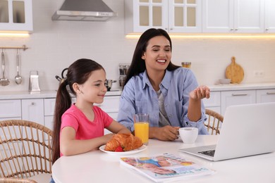 Photo of Happy mother and daughter using laptop together in kitchen. Single parenting
