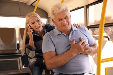 Senior man having heart attack and mature woman calling ambulance to help him in public transport