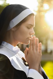 Young nun with hands clasped together praying outdoors on sunny day