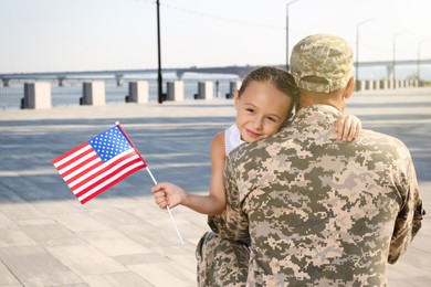 Soldier and his little daughter with flag of USA hugging outdoors
