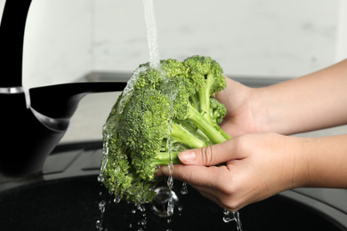 Woman washing fresh green broccoli in kitchen sink, closeup