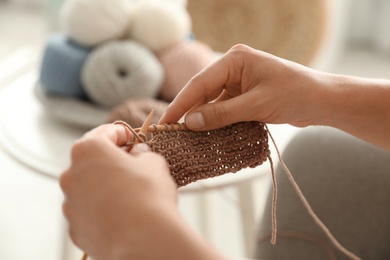 Photo of Young woman knitting with needles indoors, closeup. Engaging in hobby
