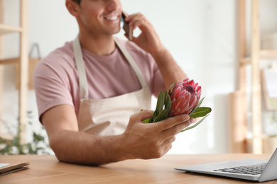 Photo of Florist with protea flower talking on smartphone in floral store, closeup