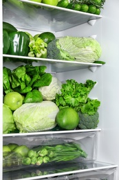 Different green vegetables and fruits on shelves of refrigerator