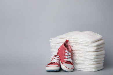 Diapers and baby shoes on light grey background. Space for text