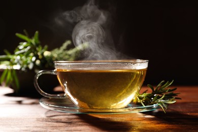 Photo of Cup of aromatic herbal tea and fresh rosemary on wooden table