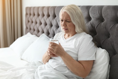 Mature woman with terrible headache holding glass of water in bed